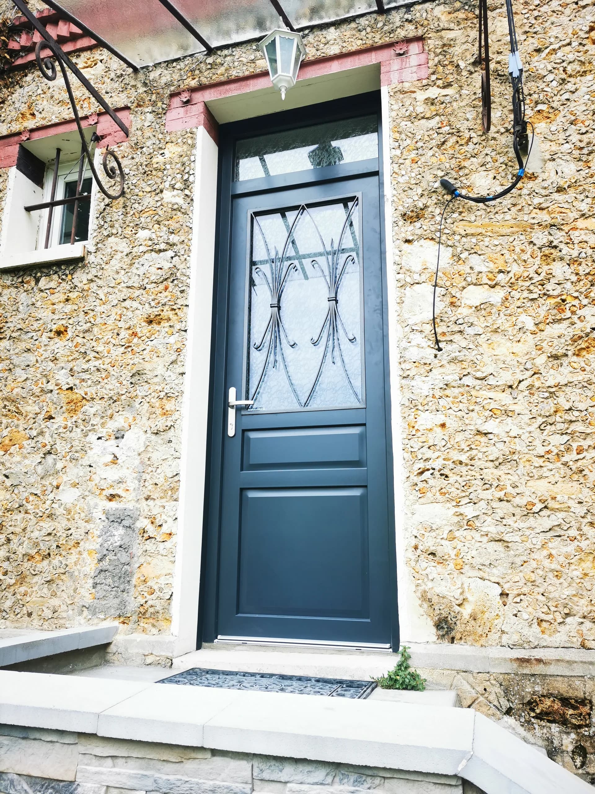 Porte d'entrée bleue avec vitrage et grille en fer forgé sur façade en pierre